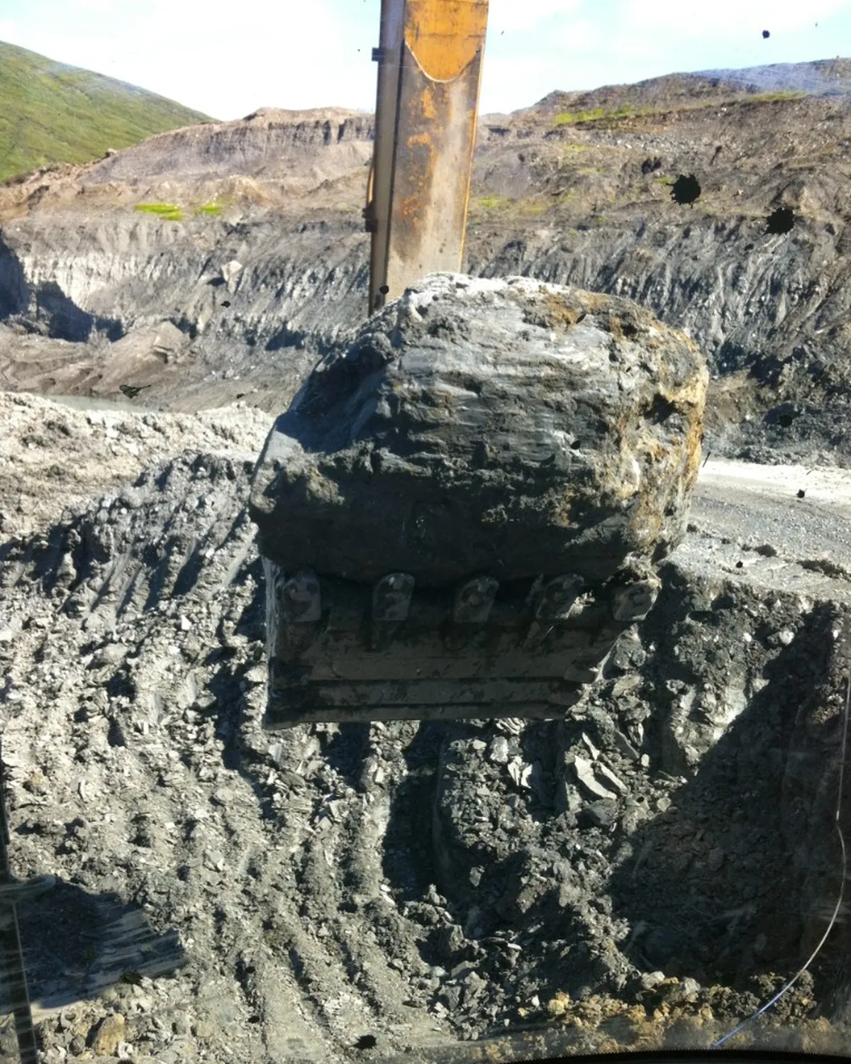 Excavator bucket lifting a large boulder in an open pit