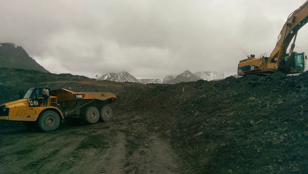 Caterpillar 740B haul truck and excavator with snowy Alaska mountains behind