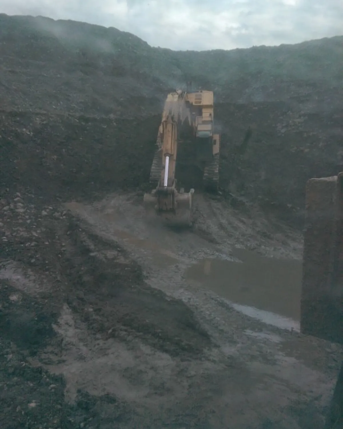 Excavator in a deep muddy mining pit