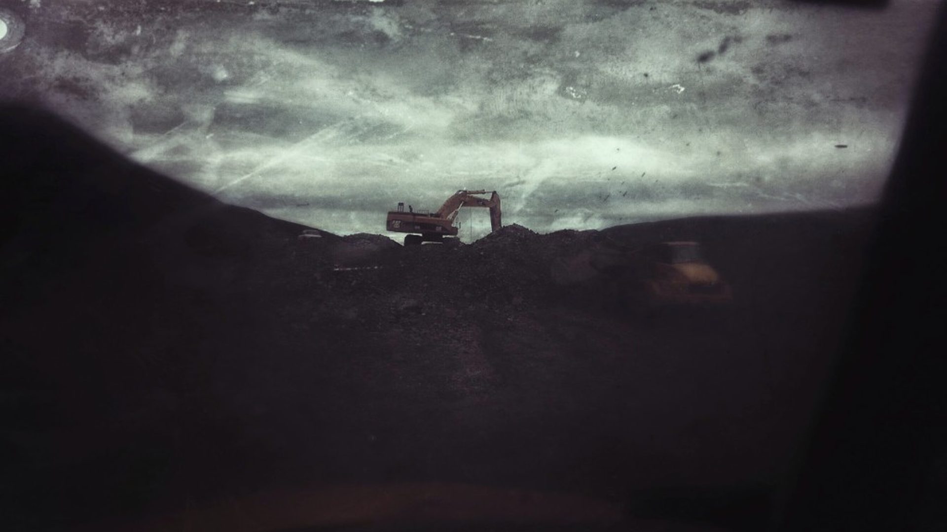 Yellow excavator on a dark mining ridge under a stormy Alaska sky