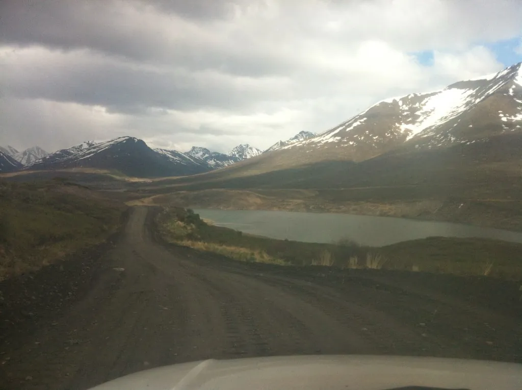 Dirt road along a mountain lake toward snow-capped Alaska peaks